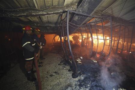 Les pompiers se tiennent près d'un feu comme ils essaient de le contrôler à l'intérieur d'une usine de confection au Bangladesh